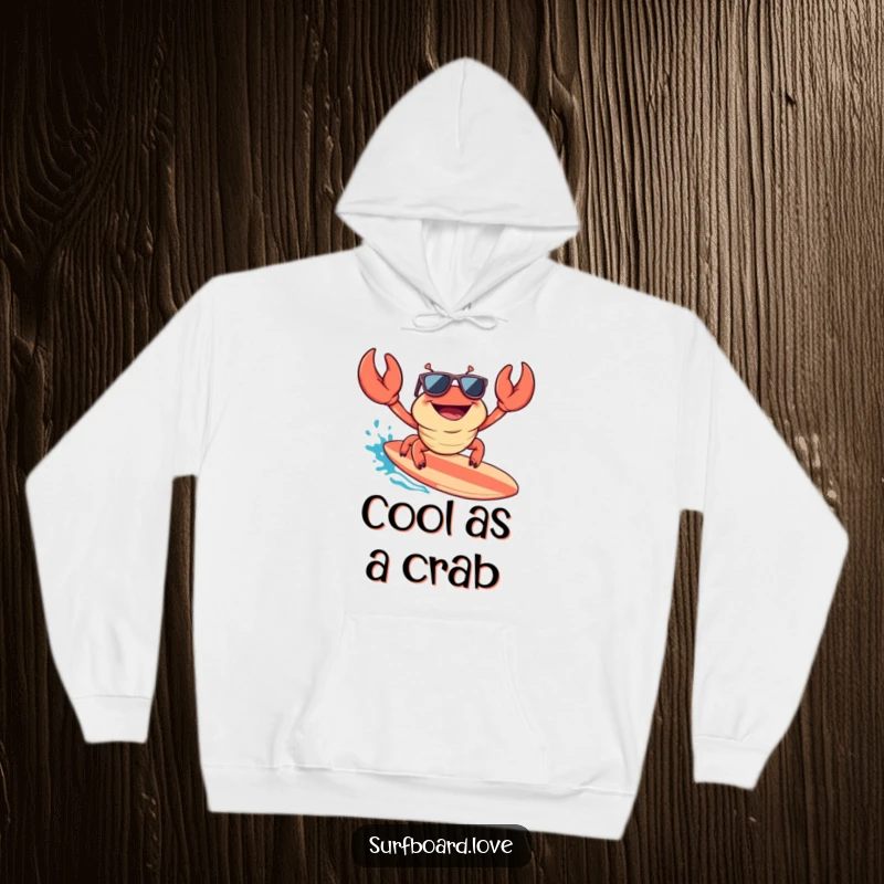 Funny hoodie with a happy crab wearing sunglasses, excitedly riding a surfboard, offering warmth and a dose of cool, humorous style.